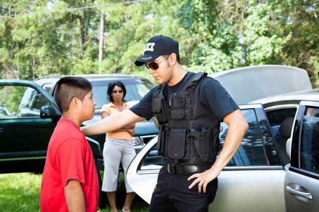 A police officer with "Police" on his cap talks to a child while a woman watches in the background. This image accompanies an article about teachers and administrators that cross the line.
